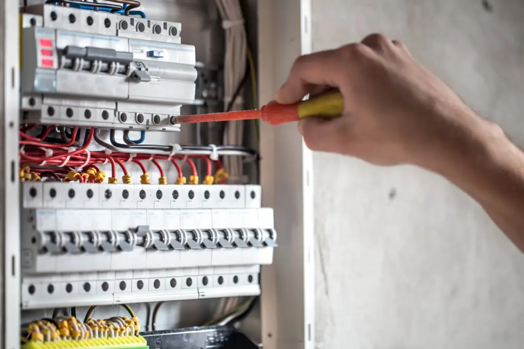 Électricien de JB Elec travaillant sur un tableau de fusibles, connectant et vérifiant les équipements électriques pour assurer la sécurité et la conformité.