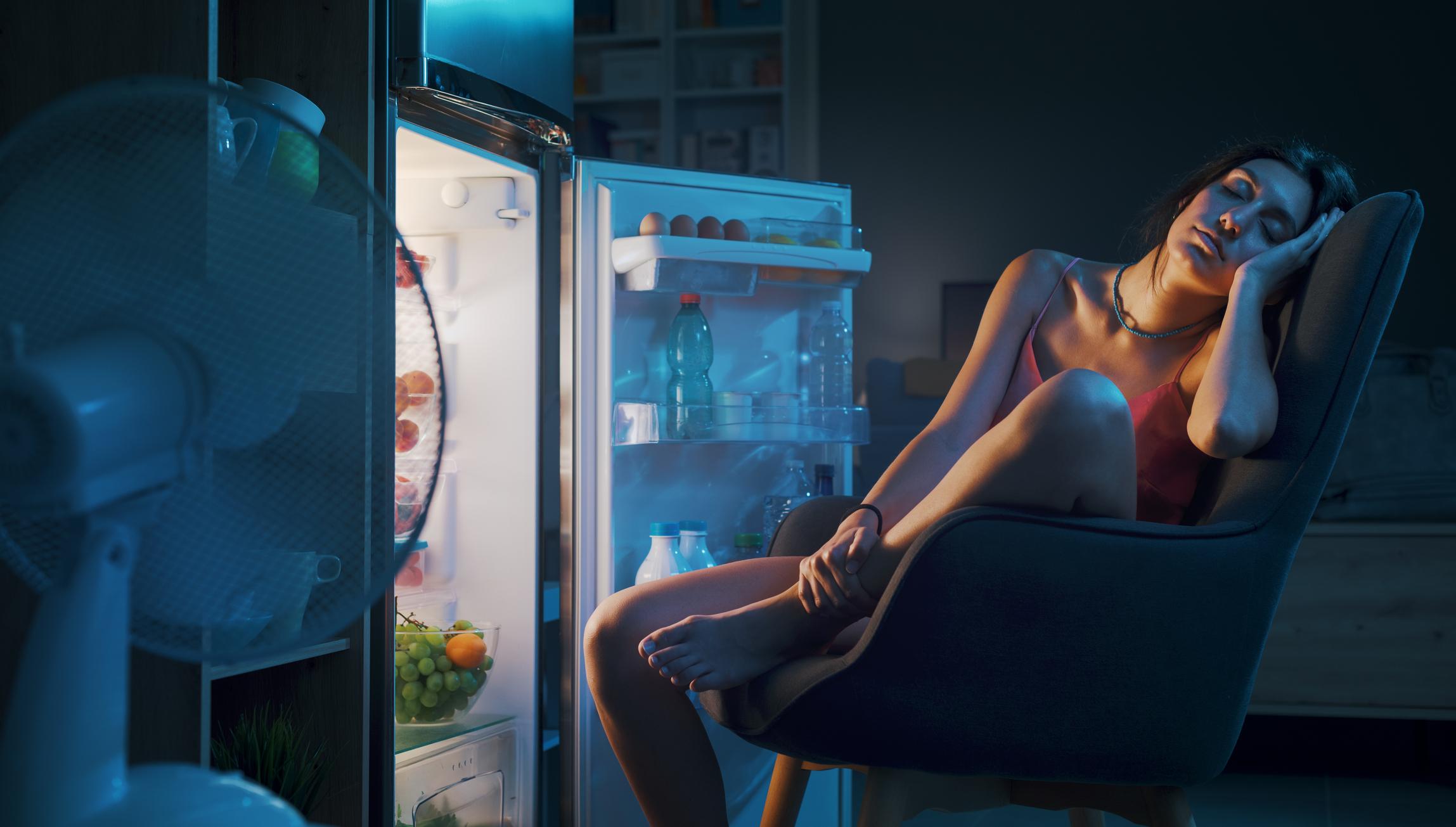 Femme souffrant de la chaleur à cause de son climatiseur en panne, obligée de dormir devant son frigo ouvert.